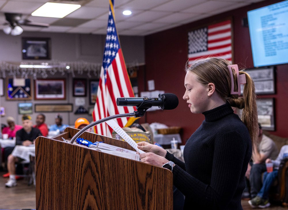 Raina Benz speaking at a podium in a classroom.