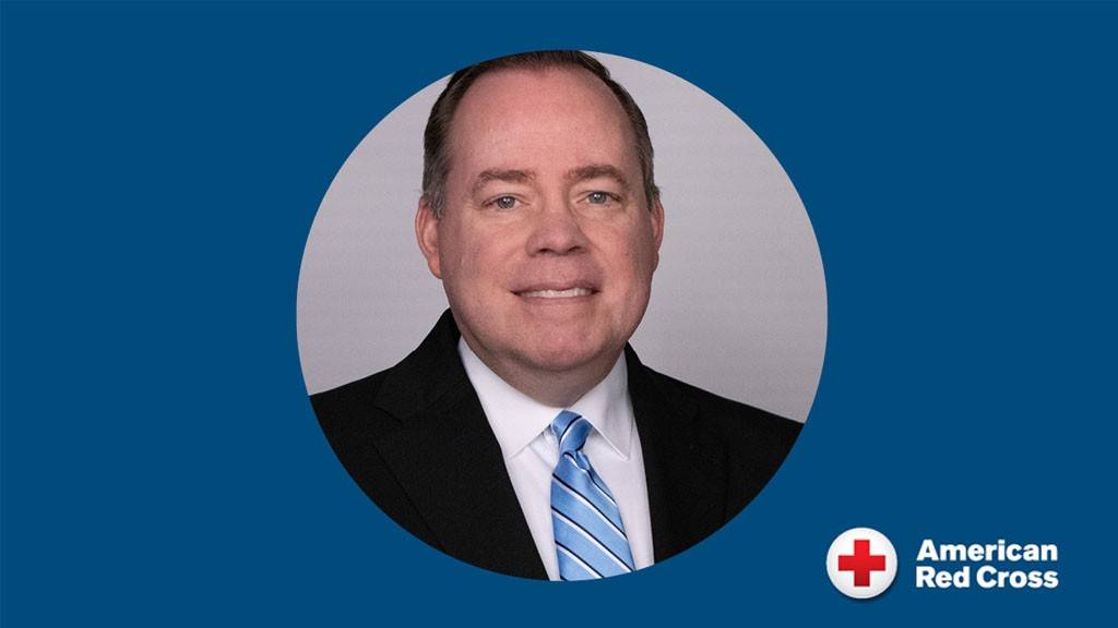 A headshot of a person in a black suit and blue striped tie.