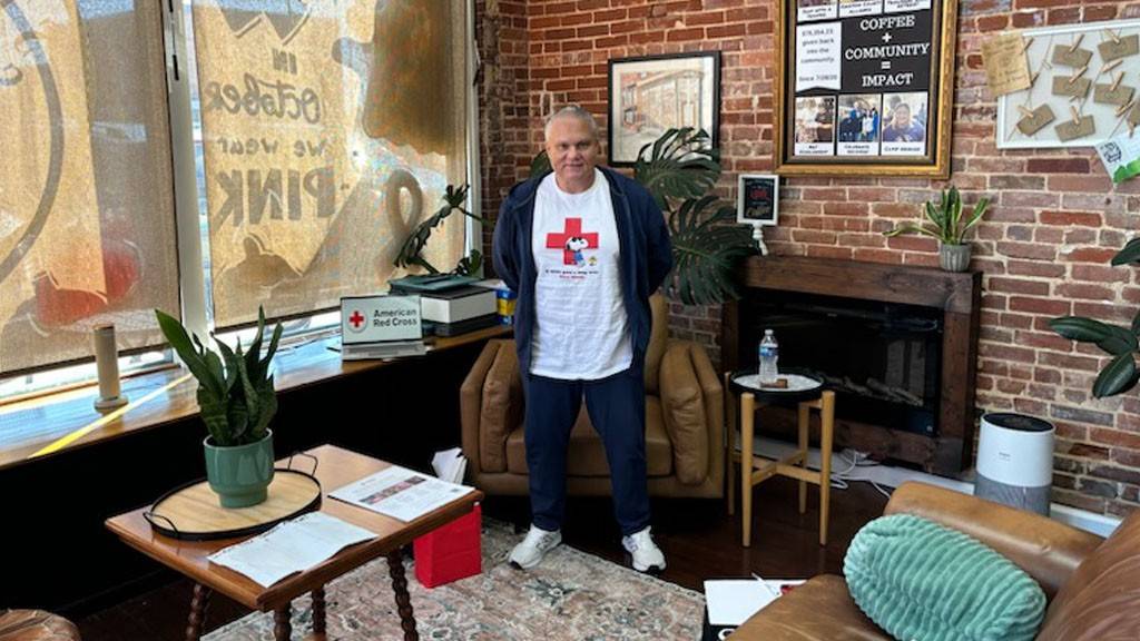 A Red Cross volunteer stands in a warmly decorated coffee shop.