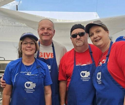 Four people in blue aprons with the words "Community Kitchen" smile at the camera.