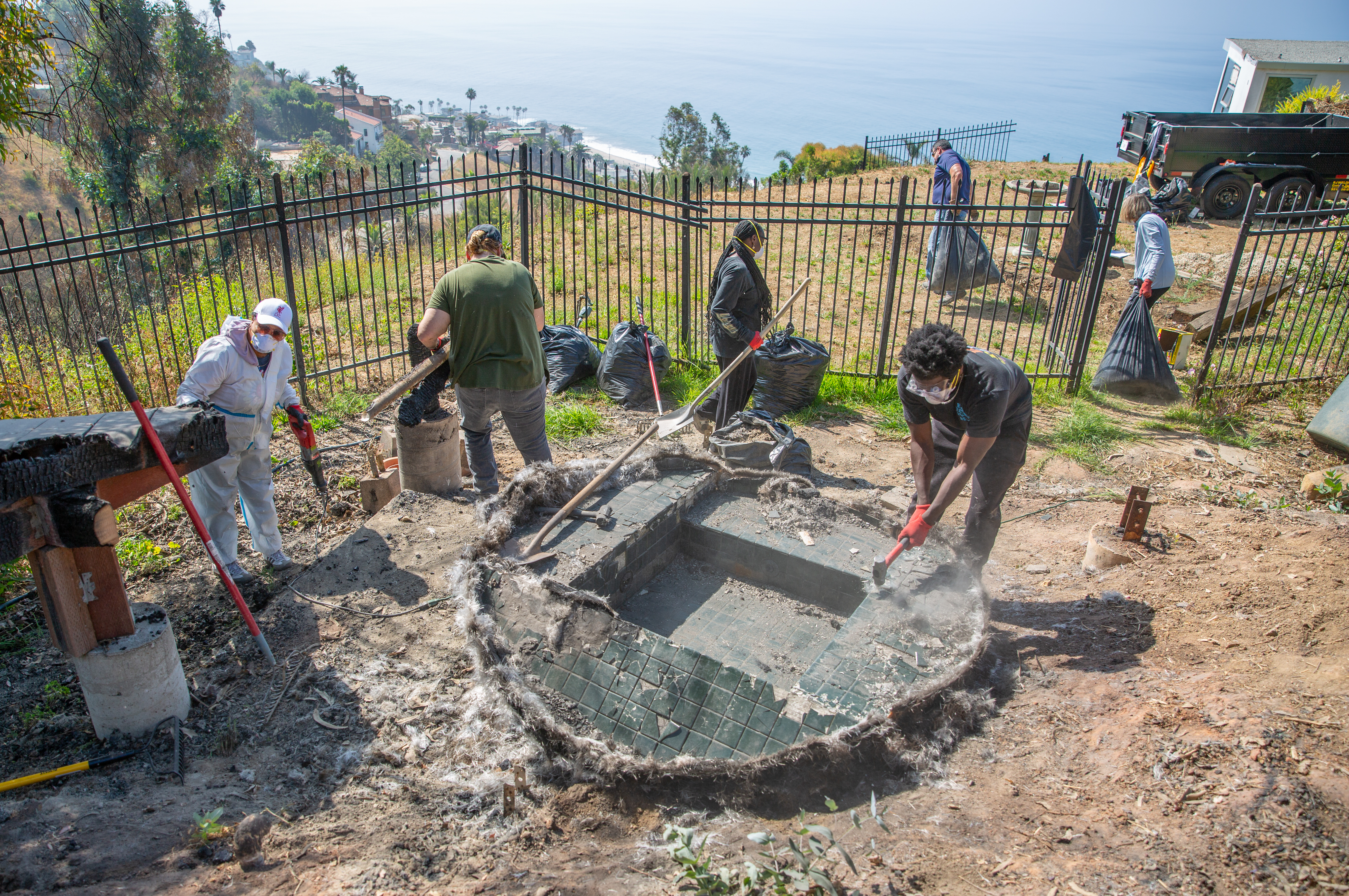 Group of six people clearning up fire debris in the backyard of a home with a view of the ocean