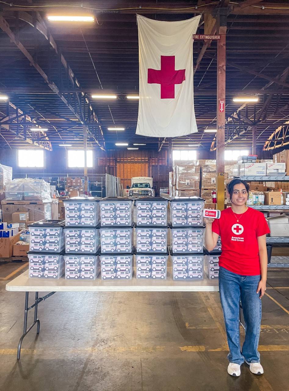 volunteer youth leader Priya Shah next to table full of packaged Emergency Response Vehicle squishy toys.