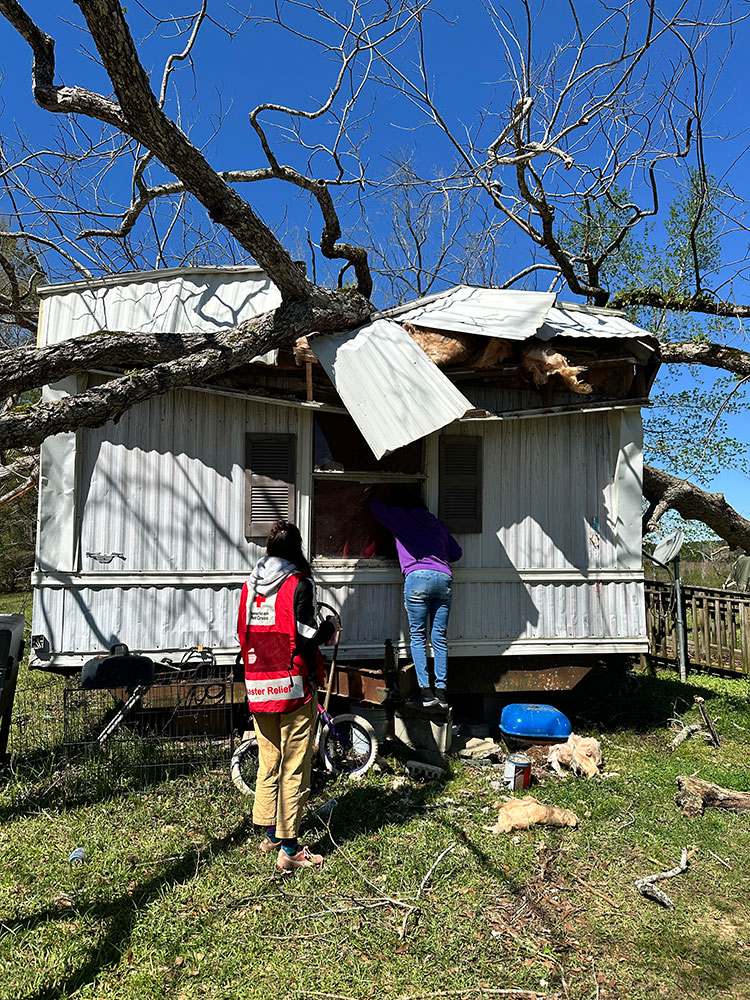 Cynthia Boykins and a Red Cross volunteer next to a house with a fallen tree on top of it.