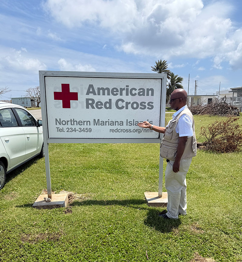Dr. Levon Aldon LeBan pointing at a Red Cross sign that's on grass.