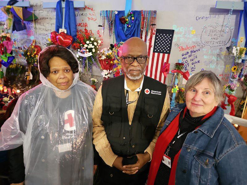 Dr. LeBan and two other Red Cross volunteers standing next to a memorial table with candles, flowers, balloons and signs.