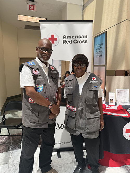 Dr. LeBan shaking hands with another Red Cross volunteer in front of a Red Cross information table.