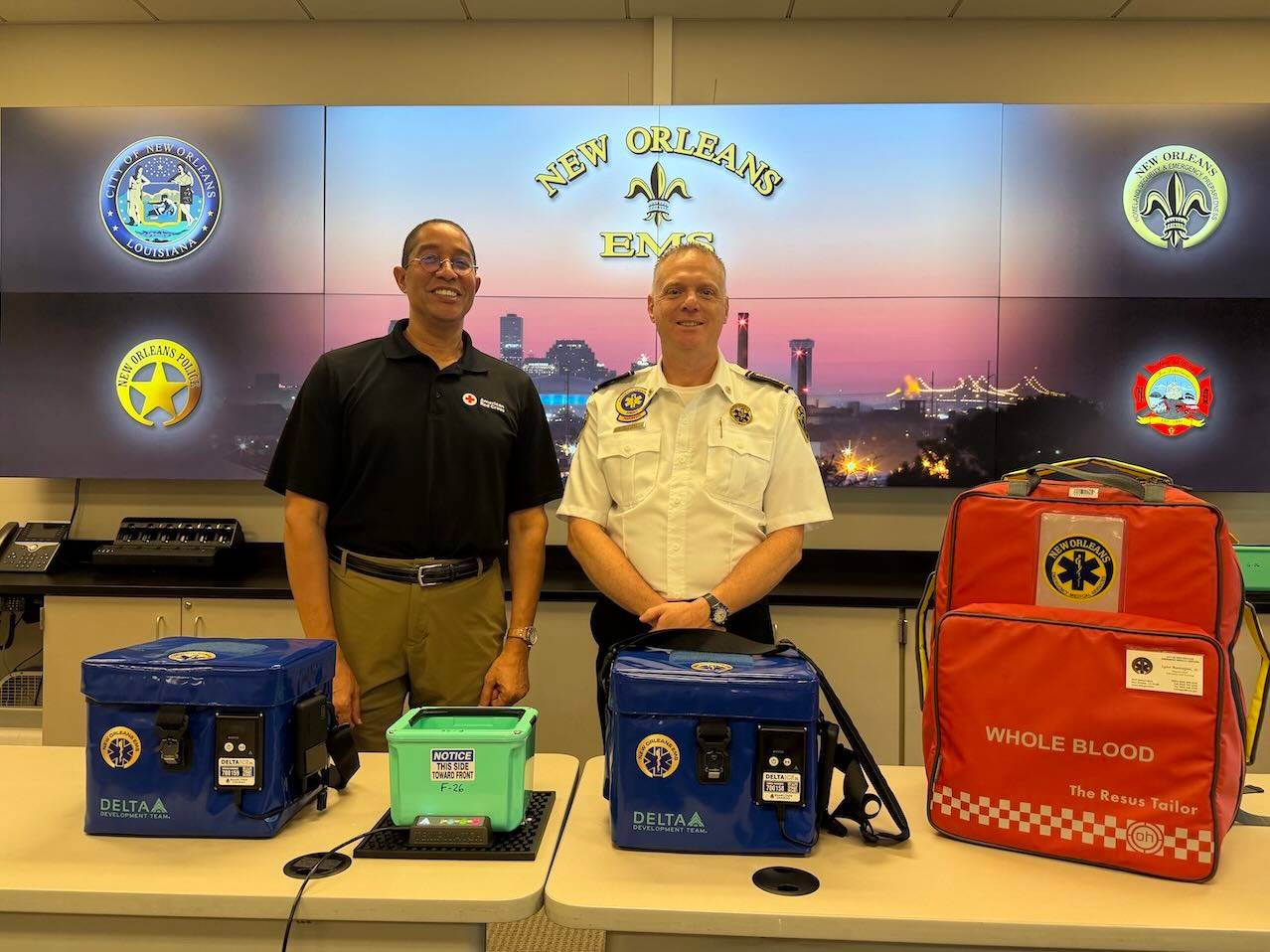 Two men stand in front of blood cooling devices. A sign reads "New Orleans EMS"