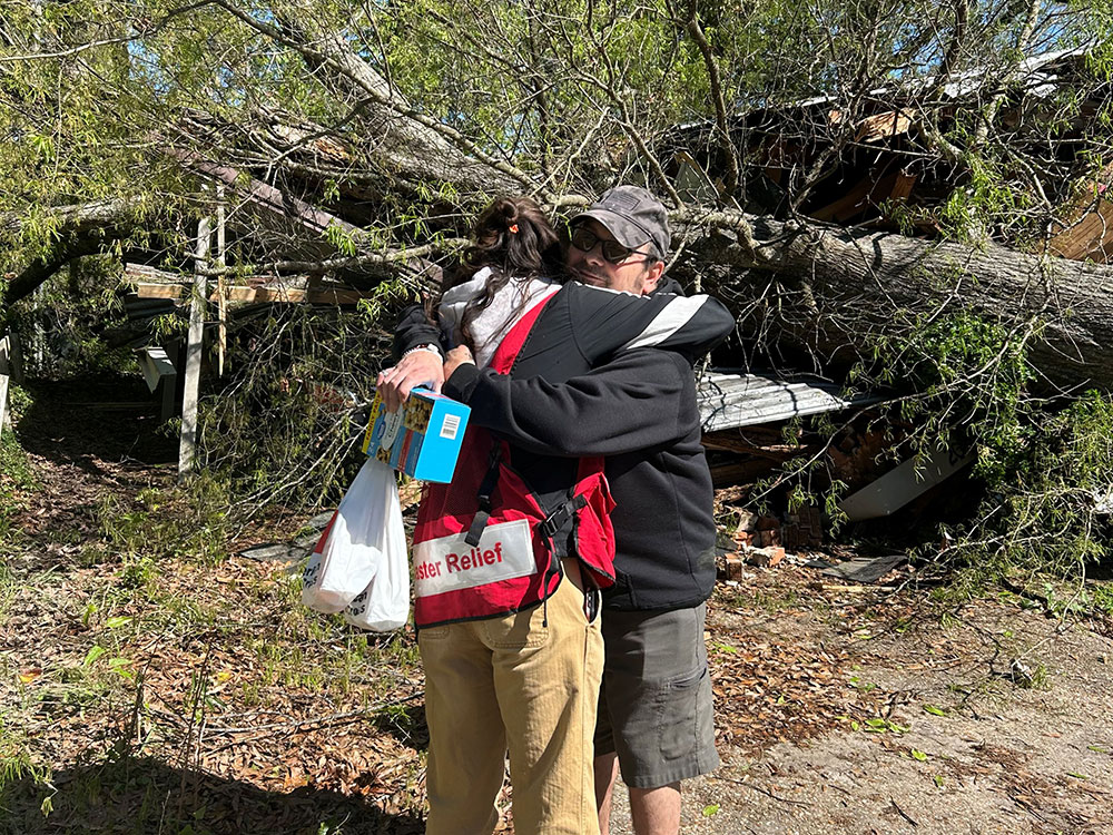 A Red Cross volunteer hugging Justin St. Mard next to a fallen tree.