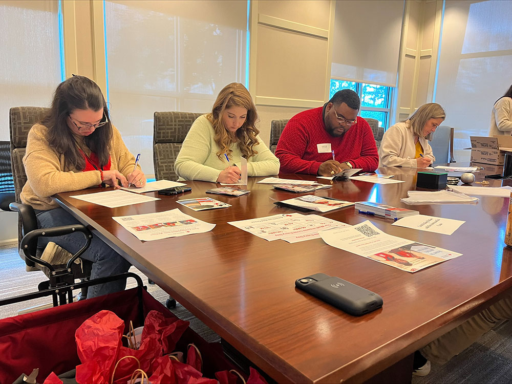 red cross volunteers and unum employees at a conference table writing in cards. 