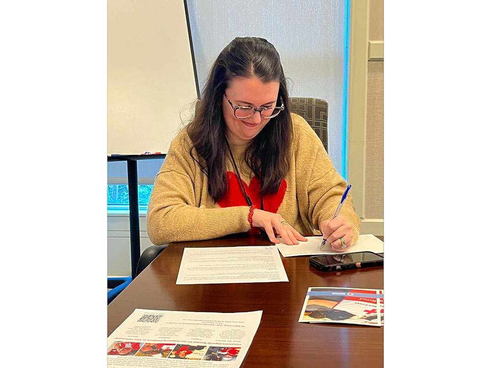 red cross volunteer at a conference table writing in a card.