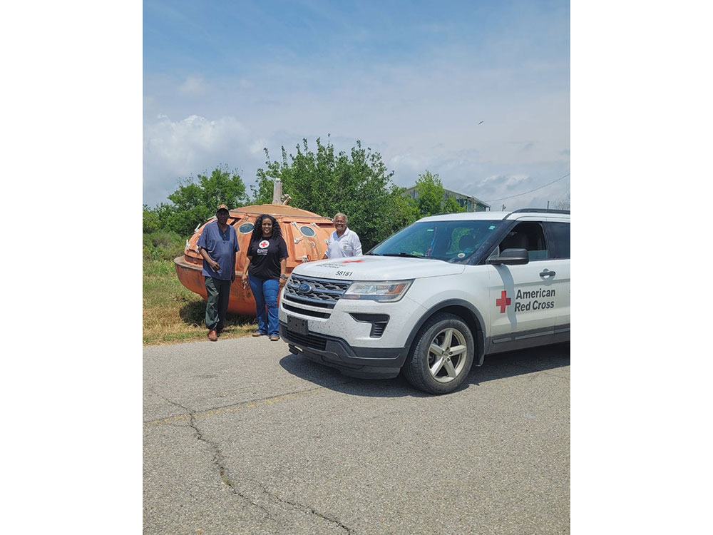 three people on the side of the road next to a Red Cross truck.