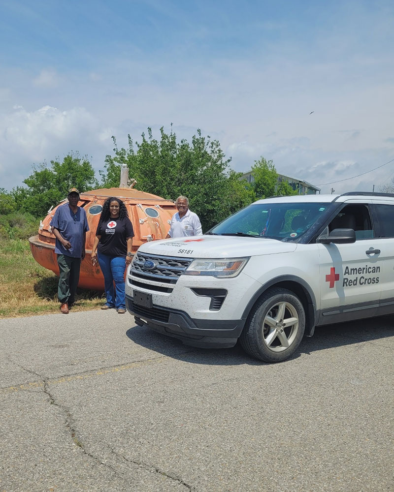 three people on the side of the road next to a Red Cross truck.