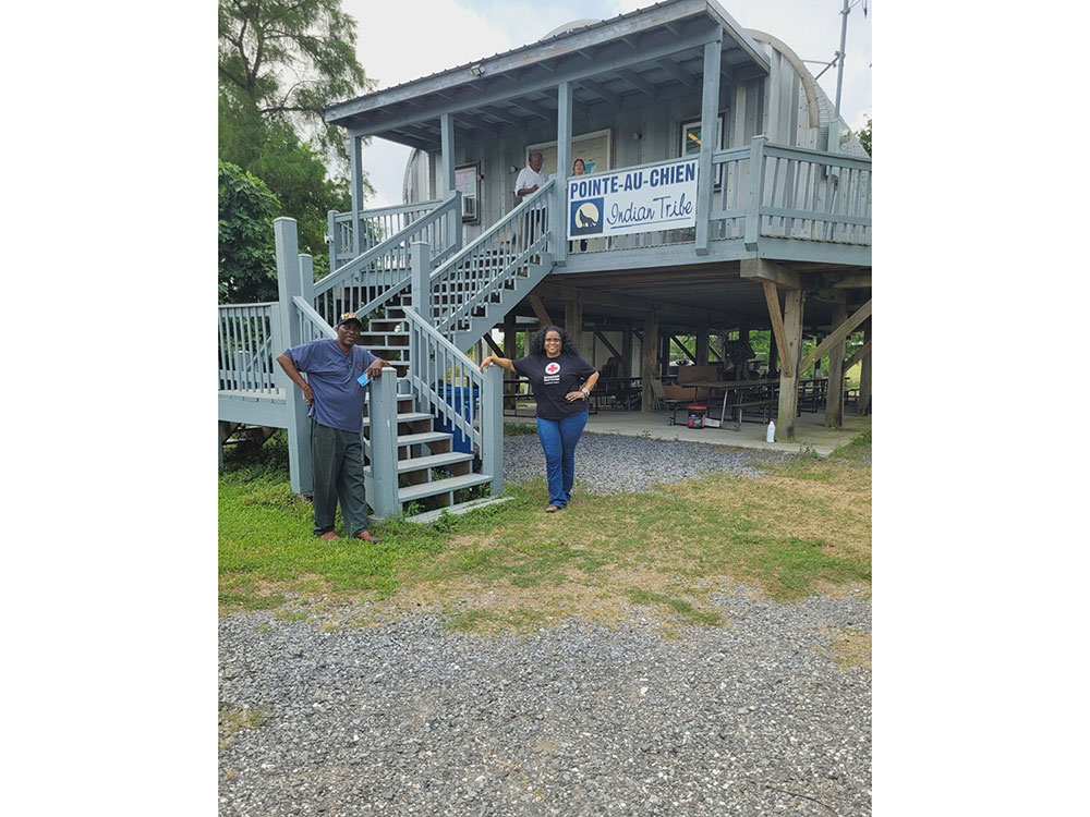 Two people pose in front of a house at the bottom of a staircase while two people stand at the front door.