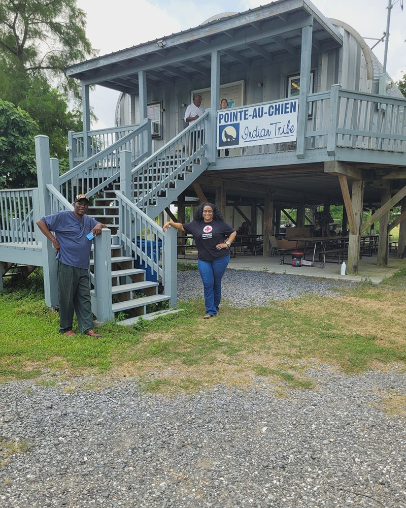 Two people pose in front of a house at the bottom of a staircase while two people stand at the front door.