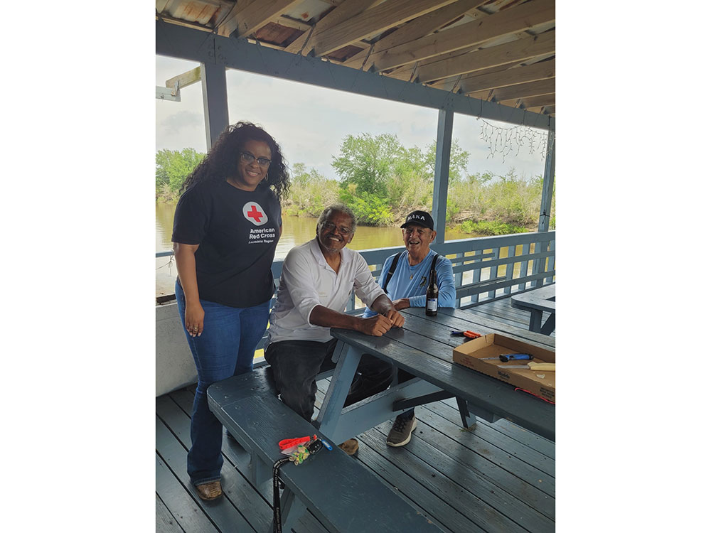 Three individuals seated at a picnic table, enjoying a view of a serene lake in the background.