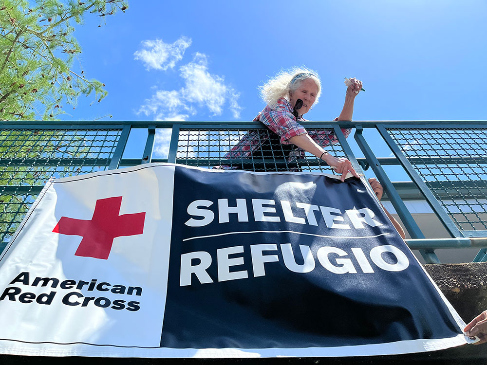 Red Cross volunteer hanging a Red Cross shelter banner on a railing.