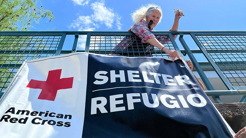 Red Cross volunteer hanging a Red Cross shelter banner on a railing.