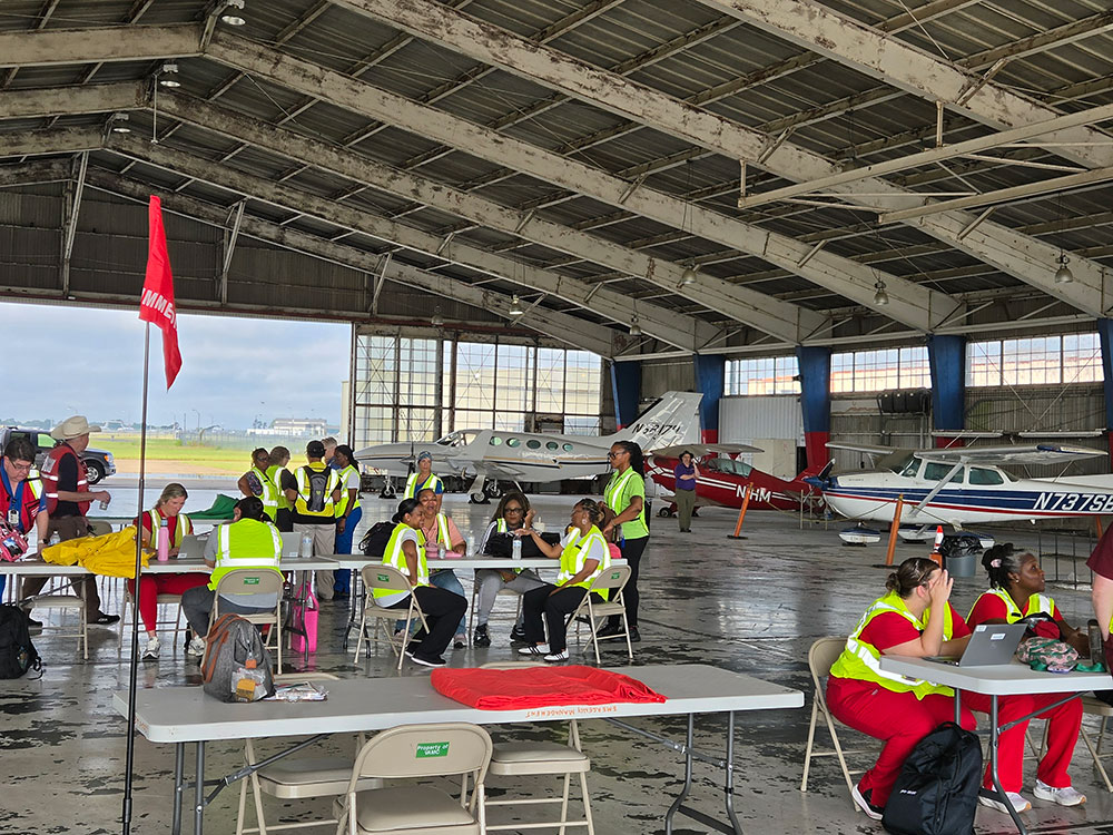 inside of an airport hanger with tables and Red Cross volunteers sitting at them.