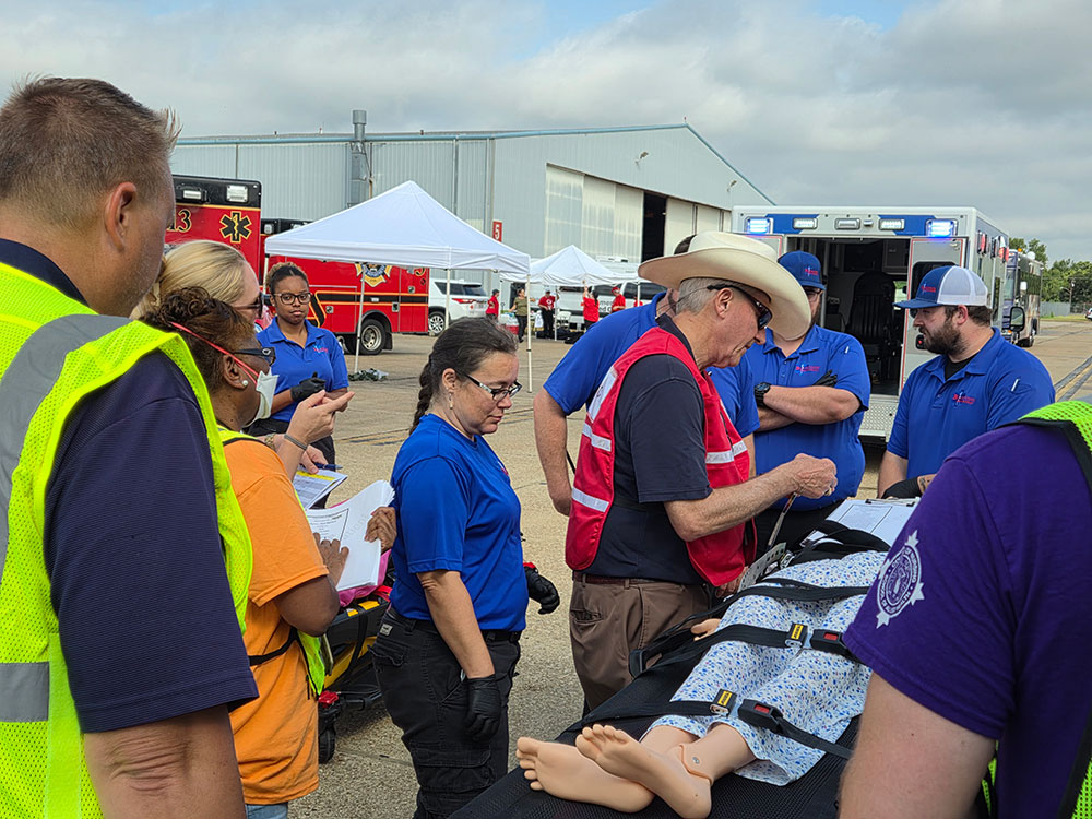 Red Cross volunteers and paramedics practicing emergency response on a manikin that's lying on a stretcher.