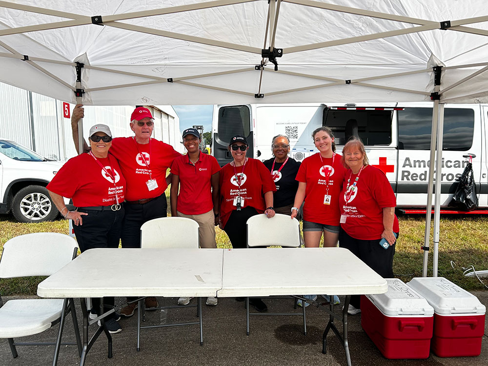 a group of Red Cross volunteers standing next to a table under a canopy.