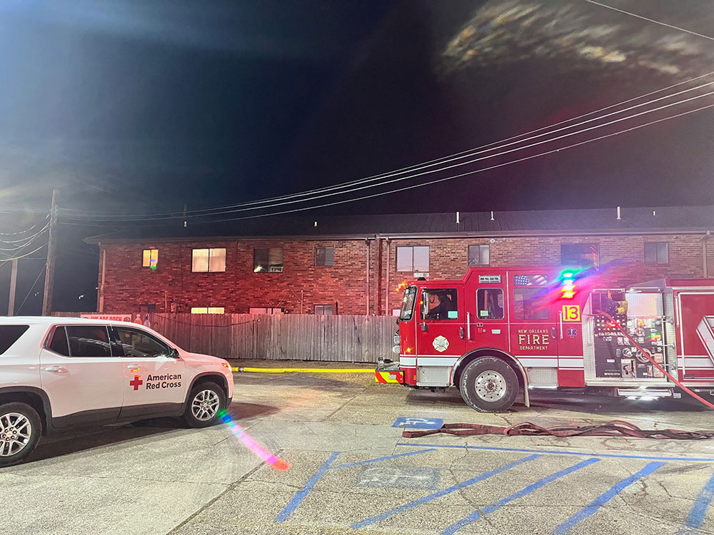 Red Cross vehicle and fire engine parked in front of burned apartments building.