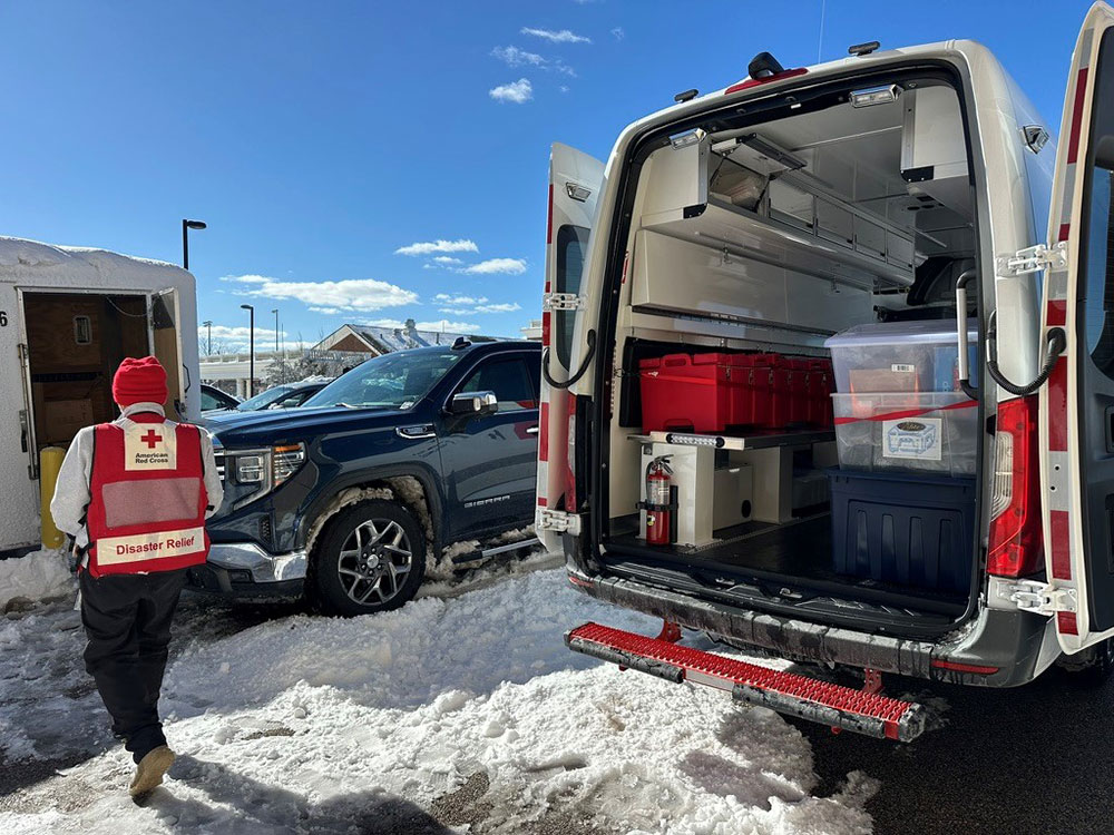 Man in Red Cross vest carries supplies into a building.