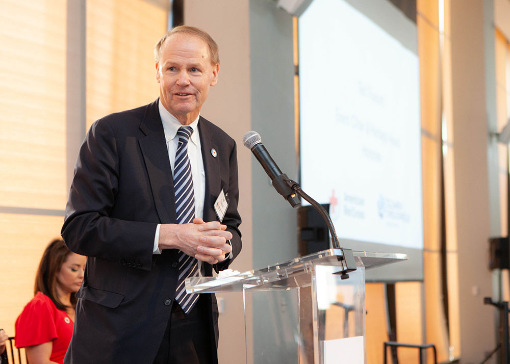 Ted Truscott in a suit and tie speaking at a podium.