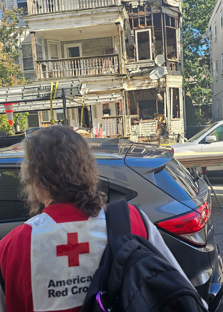 Red Cross volunteer across the street from a burned three story house.