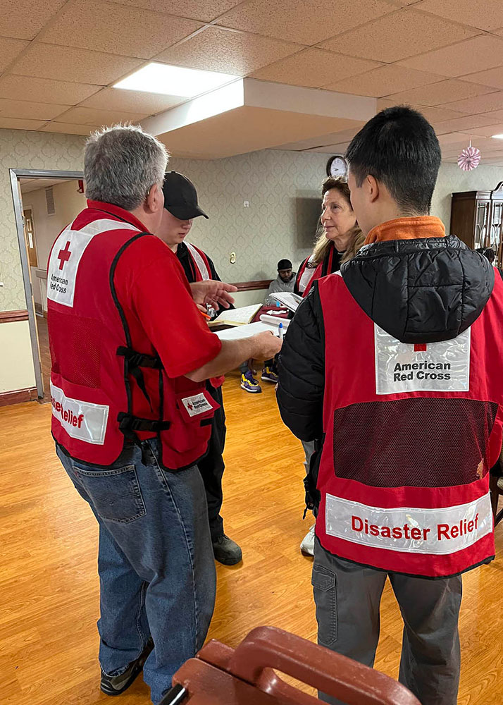 Four Red Cross volunteers in a room huddled together discussing plans.