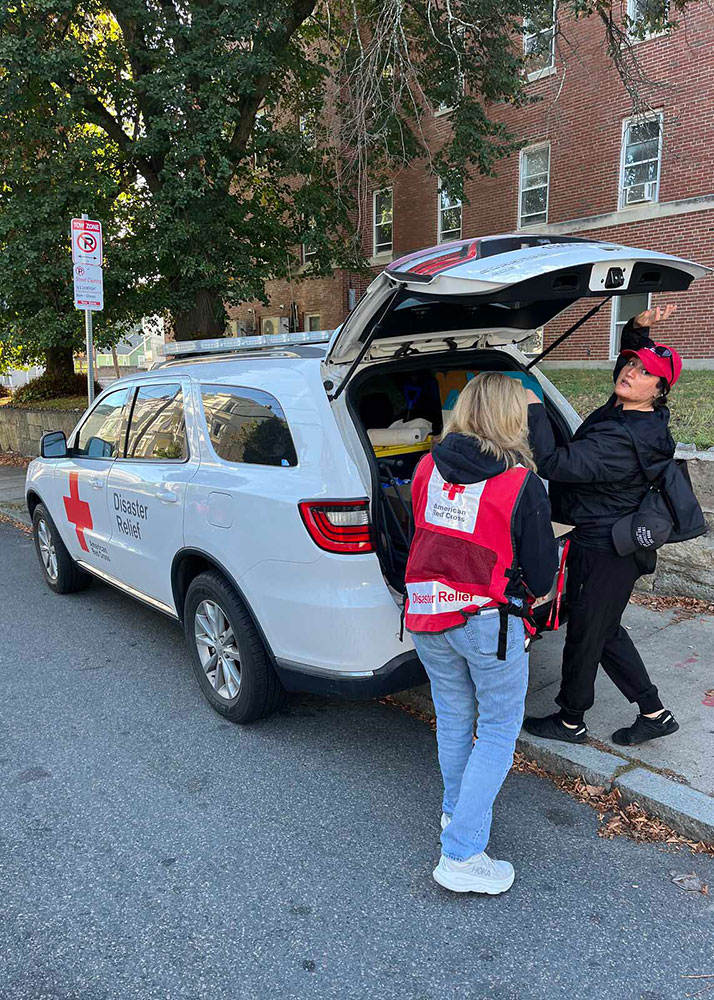 Red Cross volunteers at the back of a Red Cross van with it's back door open.