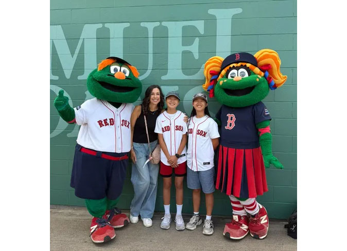 a woman and two kids with Red Sox shirts standing next to two Red Sox mascots.