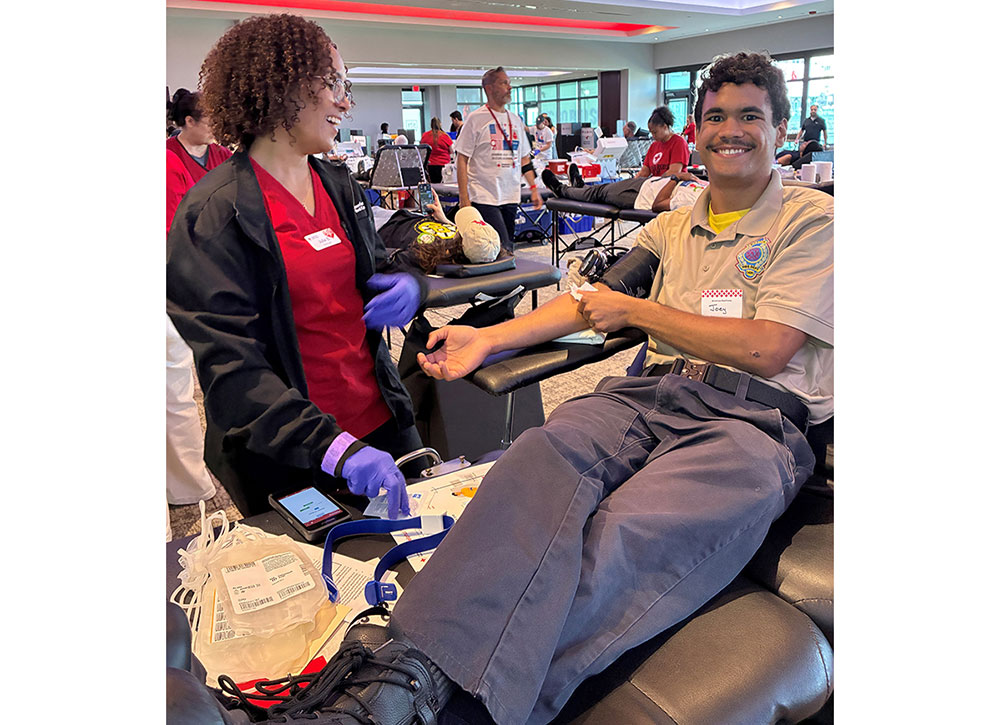 a guy in a chair donoating blood with a Red Cross nurse standing next to him.