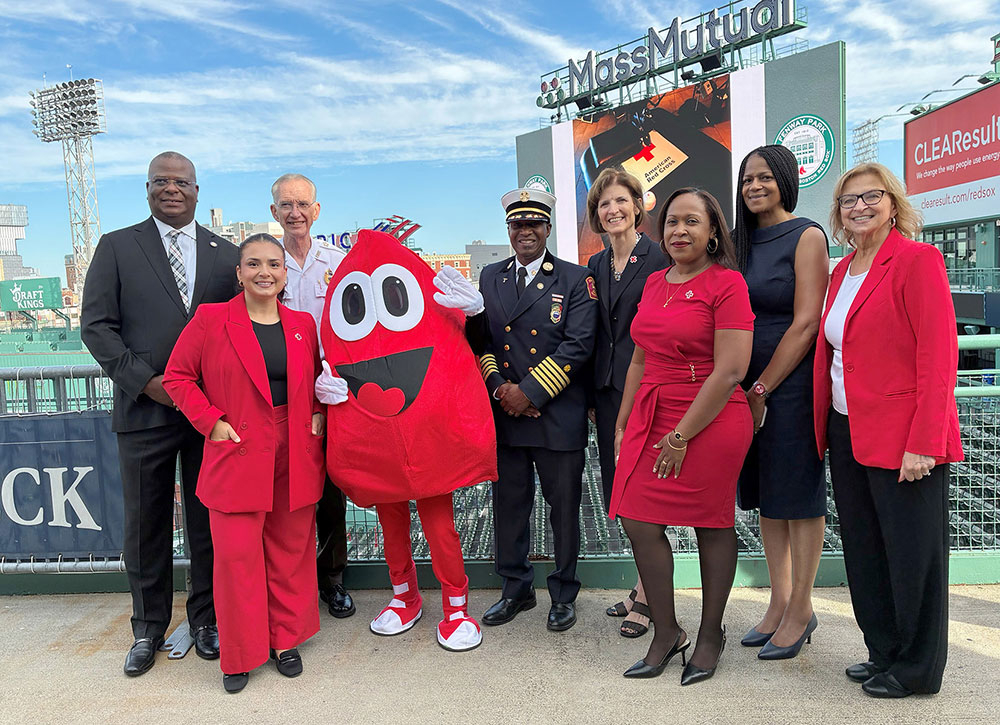 Group picture of people in dress clothing, military uniform, and a blood drop mascot in Fenway park.