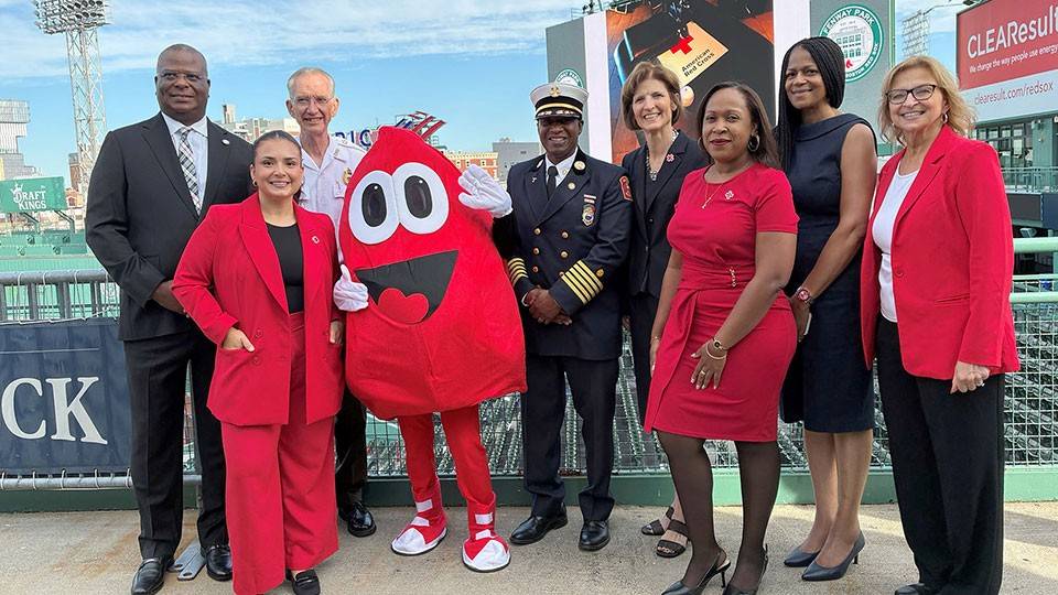 Group picture of people in dress clothing, military uniform, and a blood drop mascot in Fenway park.