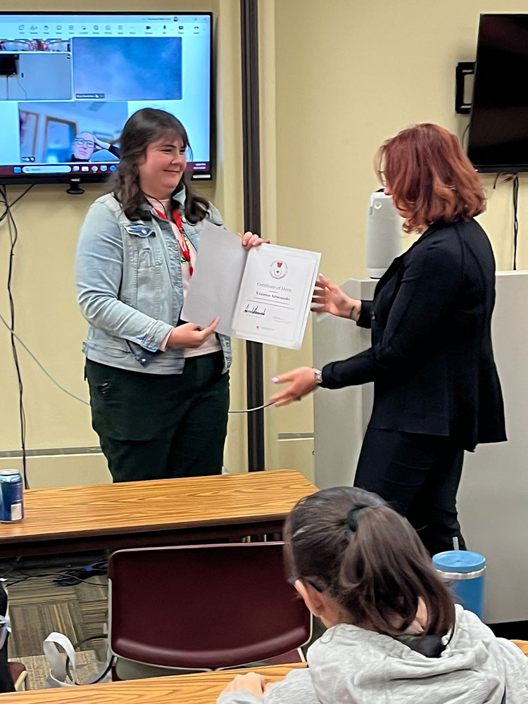 Yvonne Armando receiving a Certificate of Merit in a room full of people.