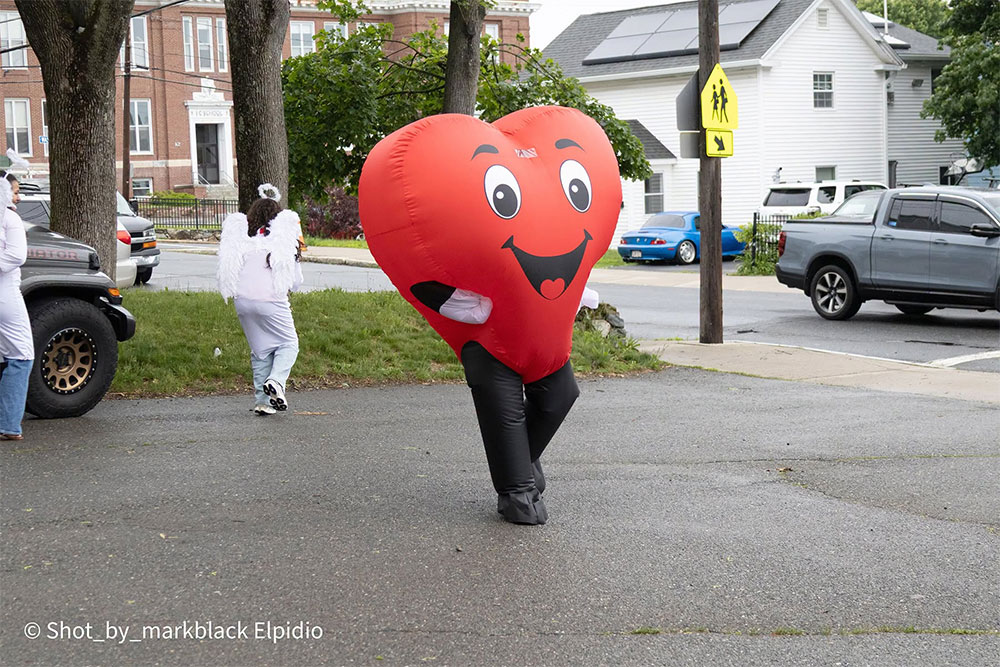 a heart shaped mascot walking in a parking lot.
