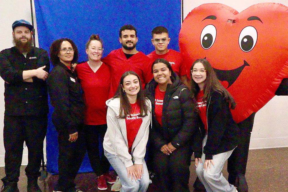 a group picture of blood donors and a heart shaped mascot.