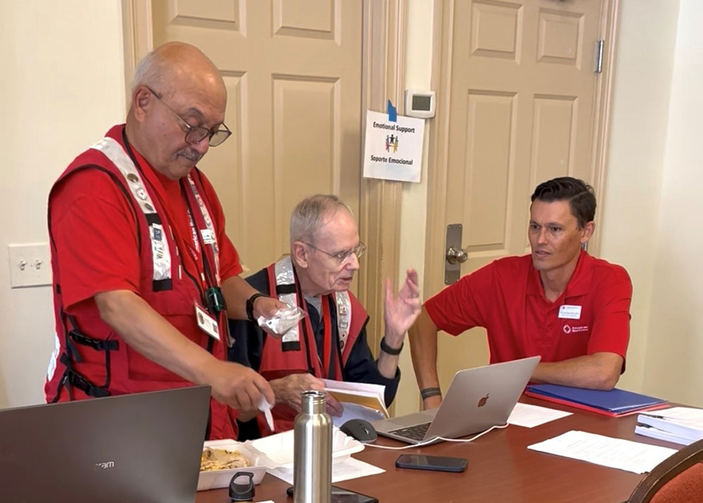 Three Red Cross volunteers in a office looking at a laptop.