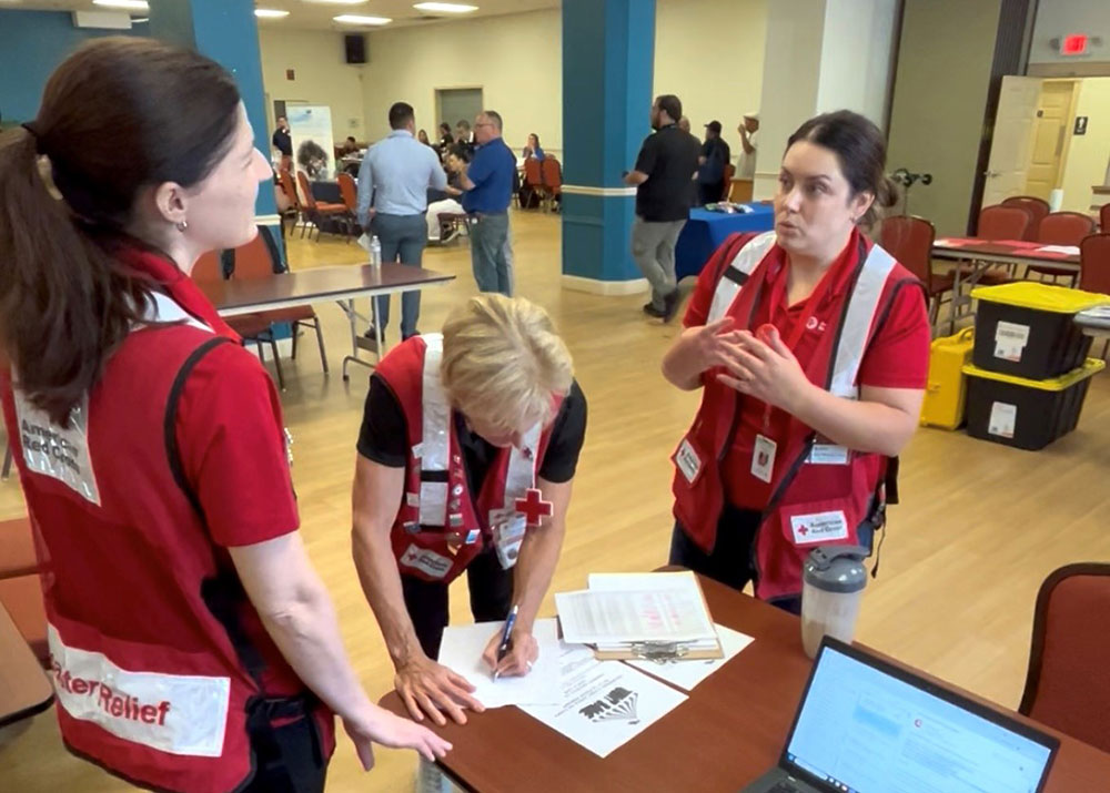 Three Red Cross volunteers in a room with tables and chairs filling out paperwork and talking to each other.