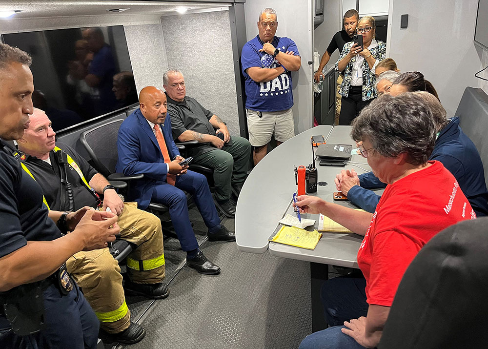 firefighters, volunteers, and other people sitting at a table talking to each other.
