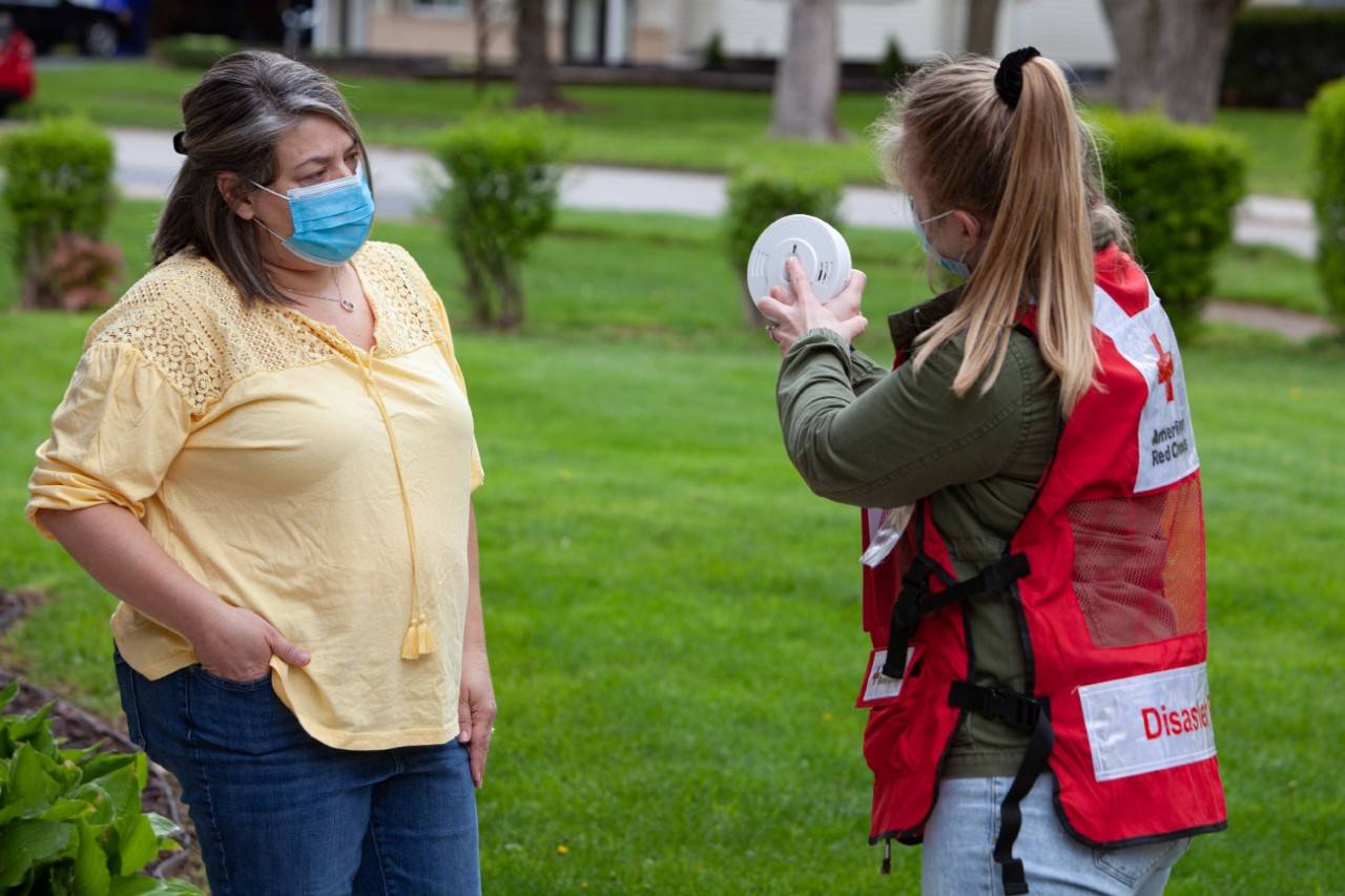 Saturday May 8, 2021. Rochester, New York.
Red Cross volunteer Jessica Cappelletti shows Rochester, N.Y., resident, Tina Mercendetti how to test smoke alarms, which members of the Gates Fire Department were installing inside her home. During the Sound the Alarm day of action on May 8, 2021, the Red Cross partnered with the Gates Fire Department to make homes safer by providing families with fire safety information and installing free smoke alarms inside. 
Photo by: Marko Kokic/American Red Cross