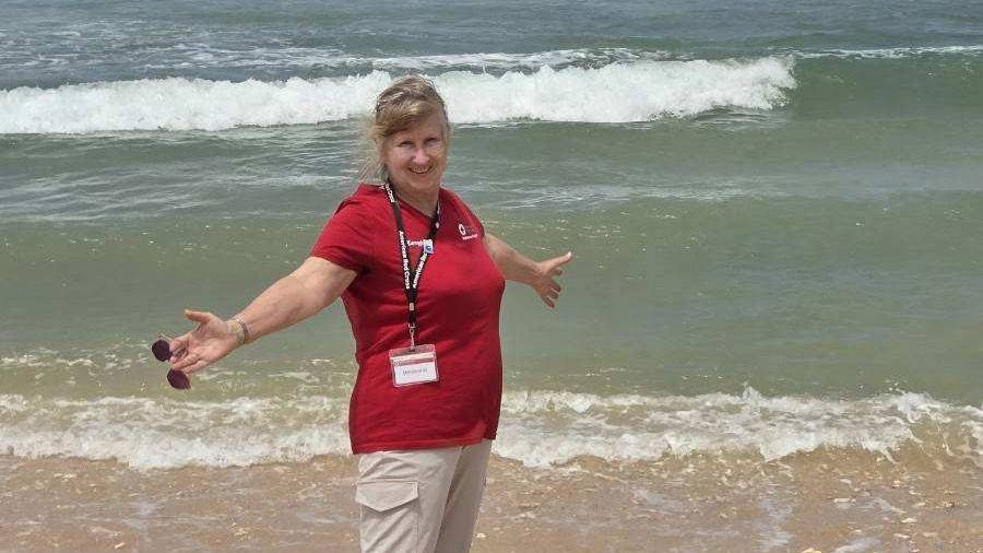 Red Cross volunteer Mary Jane Westra standing on the sand next to waves from the ocean.