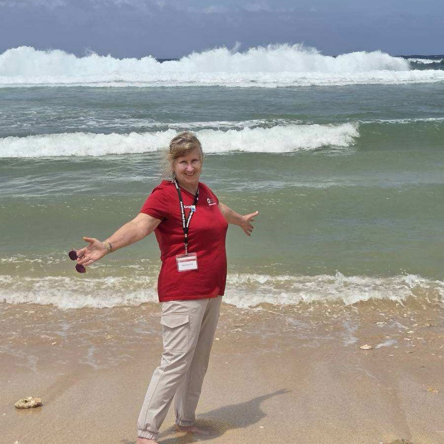 Red Cross volunteer Mary Jane Westra standing on the sand next to waves from the ocean.