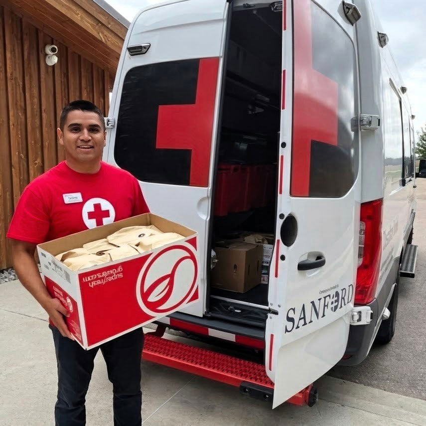 Richard Felix in a Red Cross shirt holds a box of supplies beside an open Red Cross van.