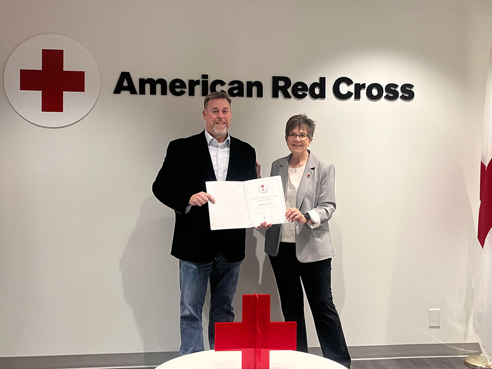 Andrew Luetje, standing next to a Red Cross employee, holding the American Red Cross Certificate of Extraordinary Personal Action.