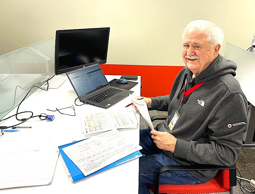 Red Cross volunteer Charlie Vires sitting at desk with a laptop and paperwork.
