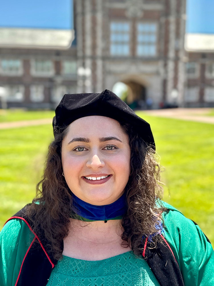 Emma Dash with head bonnet and scarf with green grass and a building in the background.