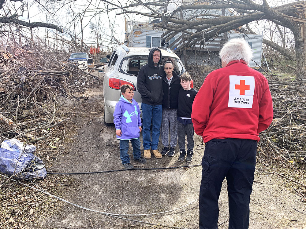 Red Cross volunteer speaking to family in front of their tornado damaged home.
