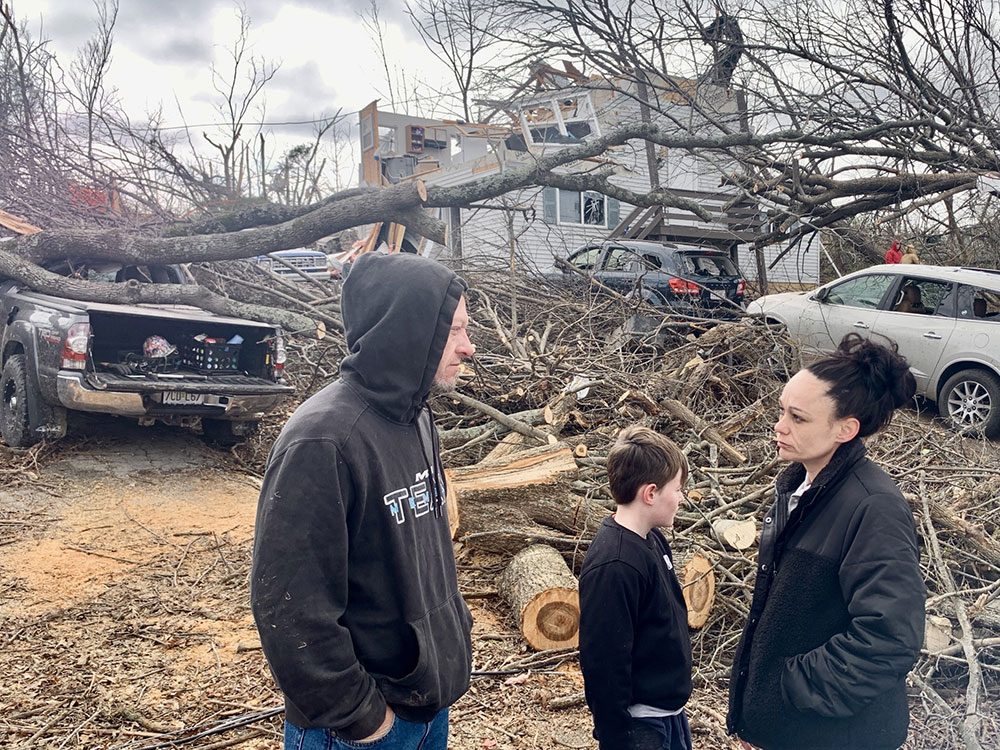 Gregory and Taylor Gerling with son Blake Clark, speaking with each other in front of their tornado damaged home.