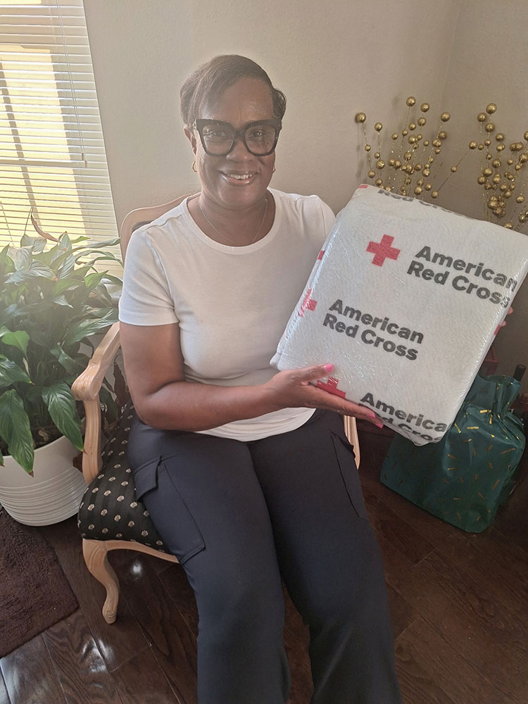 Jane Watson sitting in a chair holding a wrapped Red Cross blanket.